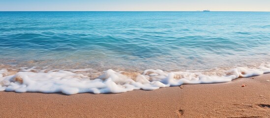 Wall Mural - A view of the shoreline at the beach as a wave rolls in, with small wet stones scattered in the sand, evoking a summer vacation atmosphere. with copy space image. Place for adding text or design