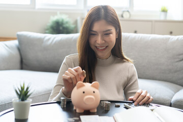 Saving money wealth concept, asian young business woman hand putting coin into piggy for saving cost, cash finance planning to spend enough money on her income for save money, payment tax, investing.