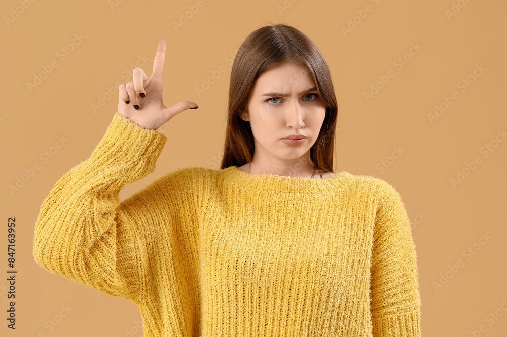 Sad young woman showing loser gesture on beige background
