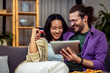 © Mediteraneo - A couple, an Asian woman and a white man, is comfortably seated in their cozy living room. They are engaged in making an online payment together