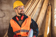 © Mediteraneo - Construction site manager standing  wearing safety vest and helmet, thinking at construction site. Young architect watching construction site with confidence.