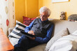 © Diego Martin/Stocksy - Senior man at home working on his digital tablet on the sofa