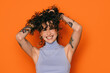 © VICTOR TORRES/Stocksy - Joyful tattooed woman with hands in curly hair on orange backdrop