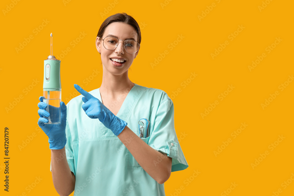 Female dentist pointing at oral irrigator on yellow background