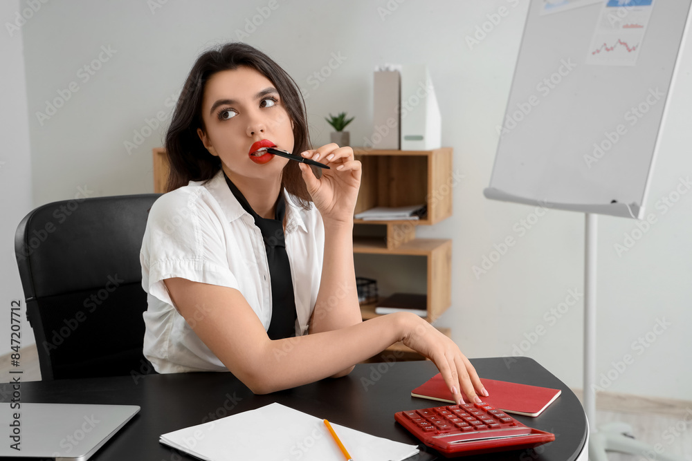 Sexy secretary with pen sitting at table in office