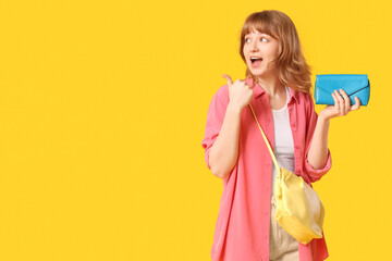 Sticker - Beautiful young woman with blue wallet pointing at something on yellow background