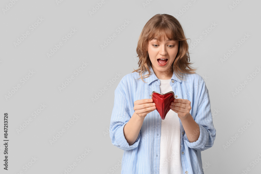 Beautiful young woman holding empty red purse on grey background