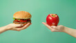 © Pavithiran - Unhealthy vs healthy food. Burger and apple in different hands on green background . Choice between fast foods and vegetables,