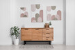 © Pixel-Shot - Interior of stylish room with wooden dresser, houseplant and pictures on white wall