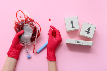 Wall Mural - Female hands in rubber gloves with blood pack, equipment for blood transfusion and calendar with date 14 JUNE on pink background. World Blood Donor Day