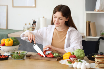 Poster - Young woman in wheelchair cutting bell pepper at home