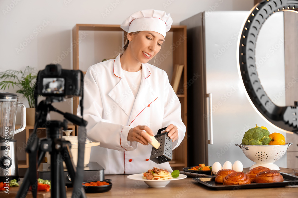 Female food blogger grating cheese on pasta while recording video in kitchen