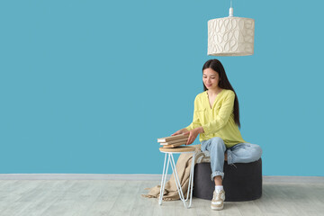 Canvas Print - Beautiful young woman reading book and sitting on pouf at home