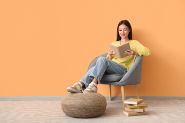 Wall Mural - Beautiful young woman reading book and sitting on cozy armchair at home
