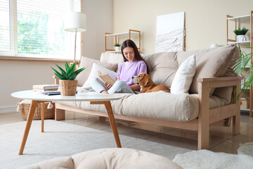 Sticker - Young woman reading book with cute Beagle dog on sofa in living room