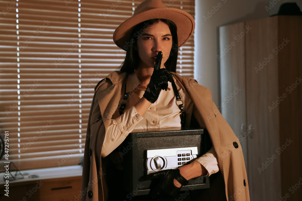 Female spy with safe showing silence gesture in office at night