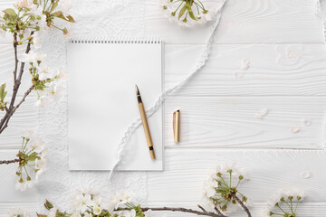 Wall Mural - Guest list. Notebook, pen, spring tree branches with beautiful blossoms and lace ribbons on white wooden background, flat lay. Space for text