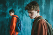© HecoPhoto - Thoughtful teenage boy wearing wireless earphones looking down with a backpack against a blue background