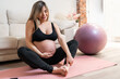 © Alvaro Lavin/Stocksy - Pregnant woman sitting on yoga mat.