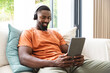 © Wavebreak Media - Young African American male relaxing on couch, using tablet and wearing headphones