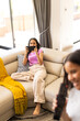 © Wavebreak Media - Two young biracial sisters relaxing, one using smartphone while other holds a remote, at home