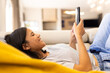 © Wavebreak Media - Biracial young woman relaxing on couch, smiling while looking at her smartphone, at home