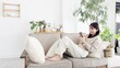 © mapo - ソファでくつろぎながらスマホを見る女性