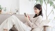 © mapo - ソファでくつろぎながらスマホを見る女性