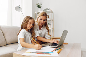 Mother and daughter collaborating on a laptop at a table adorned with colorful pencils, fostering creativity and learning