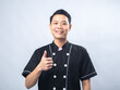 © Daniel - Smiling young man in a black chef uniform, giving a thumbs-up gesture against a plain light gray background. The man exudes confidence and positivity,