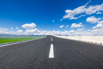 Wall Mural - Asphalt highway road and green meadow with mountain nature landscape under blue sky