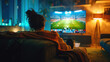 © Mehran - A person relaxes in their armchair at home, watching a sports game on their large television.