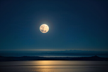 Wall Mural - a full moon hangs in the dark night sky, casting a soft glow on the rippling ocean waves