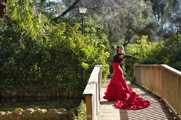 Canvas Print - Young, beautiful, brunette woman in black shirt and red skirt, dancing flamenco in the middle of a wooden bridge inside a park. Flamenco concept, dance, art, typical Spanish.