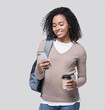 © kite_rin - Young beautiful woman with backpack looking at smart phone and holding coffee cup isolated on gray background, Smiling student girl going on travel