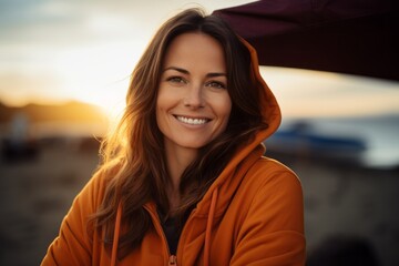 Portrait of a smiling woman in her 30s wearing a zip-up fleece hoodie isolated in relaxing hammock on the beach background
