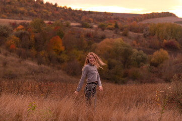 Wall Mural - Young attractive blonde woman standing on the hill at sunset	