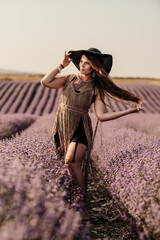 Canvas Print - A woman is standing in a field of purple flowers, wearing a black dress and a black hat.