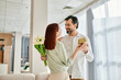 © LIGHTFIELD STUDIOS - A man with a beard is giving a gift to a beautiful redhead woman in a stylish living room.