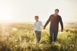 © Lyndon/peopleimages.com - Holding hands, walking and dad with child in nature at sunset for bonding together on vacation. Happy, farm and father with boy kid on adventure, holiday or weekend trip in agriculture countryside.