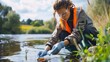 © Elmira - A female biologist in a safety vest and gloves conducts a water quality assessment in a river. She is carefully collecting a sample of water for analysis