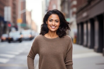 Wall Mural - Portrait of a happy indian woman in her 30s wearing a cozy sweater isolated in bustling city street background