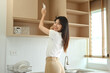 © Prathankarnpap - Happy young Asian woman arranging plates in an overhead kitchen cabinet