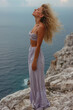 © pisan - Woman Enjoying Serenity on Rocky Cliff Overlooking the Ocean with Windblown Hair and Summer Outfit