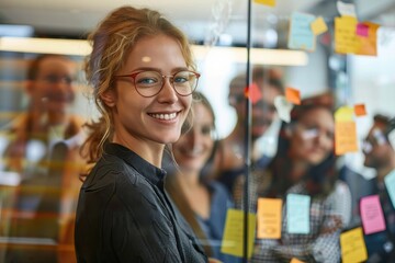 Smiling woman with glasses in front of post-it covered glass, in a collaborative workspace