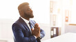 © Prostock-studio - African entrepreneur praying in office before important deal, sitting in front of laptop, copy space