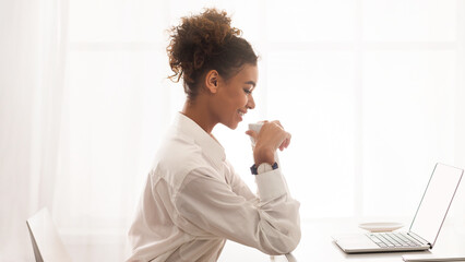 Aufkleber - African American woman is sitting in front of a modern laptop computer, focused on the screen as she types and clicks. She appears to be working or studying intently in a home or office setting.