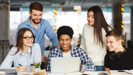 Aufkleber - A diverse group of people are gathered around a table indoors. They are actively engaged and focused on a laptop screen, likely discussing work-related matters or collaborating on a project.
