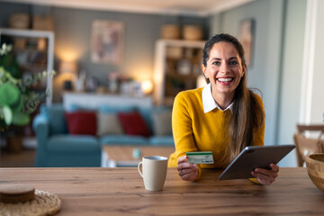 Wall Mural - Successful woman entrepreneur smiling at camera while holding credit card and digital tablet pc at home.