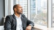 © mashimara - Pensive businessman in a suit gazing thoughtfully out of a window in a high-rise office, contemplating the cityscape. Reflection and focus in a corporate setting.